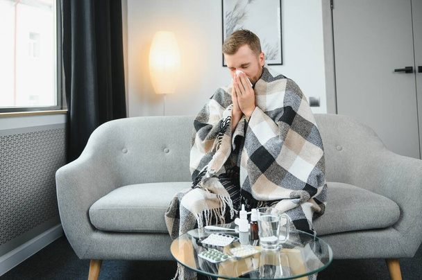 Sick man on sofa at home and blowing nose. - Fotó, kép