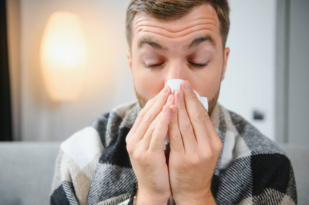 Sick man on sofa at home and blowing nose. - Foto, Imagen