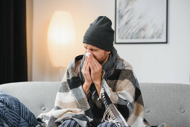 Sick man on sofa at home and blowing nose. - Foto, Bild
