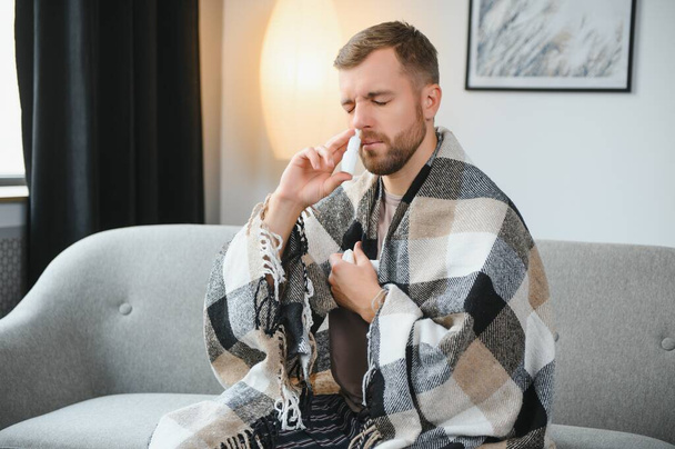 Sick man with nasal spray and paper tissue at home. - Foto, afbeelding