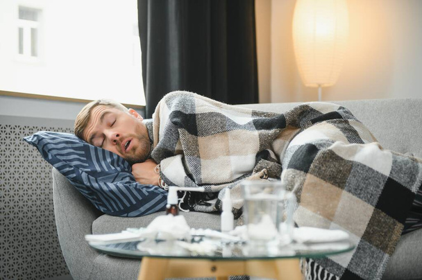 It's cold at home in wintertime. Man freezing in his house in winter because of broken thermostat. young guy wrapped in woolen plaid shivering while sitting on sofa in living room interior. - Foto, Bild
