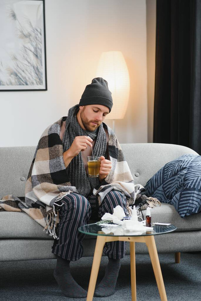 A sick man sits at home on a gray sofa with a blanket. Illness, protection, coronavirus, illness, flu. - Fotoğraf, Görsel