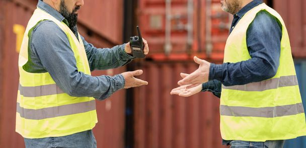 Männliche Arbeiter und Teams in Schutzuniformen und Helmen benutzen Walkie-Talkies, arbeiten am Logistikkran mit Containerstapeln, kontrollieren die Verladung von Transportgütern und die Speditionsindustrie. - Foto, Bild