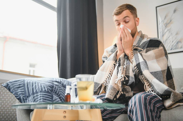 Sick man on sofa at home and blowing nose. - Foto, imagen