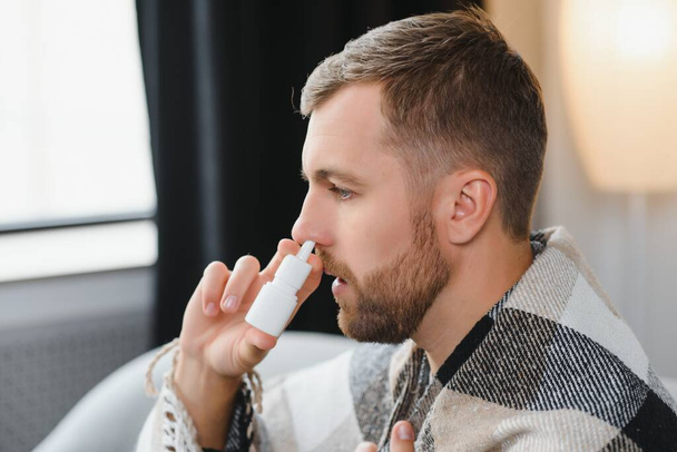 Sick man with nasal spray and paper tissue at home. - Фото, зображення