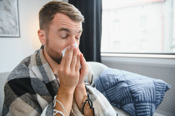 Uomo malato sul divano a casa e soffiando il naso. - Foto, immagini