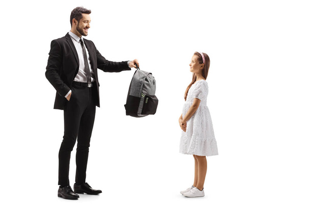 Full length profile shot of a father giving a backpack to a girl isolated on white background - Foto, Imagem