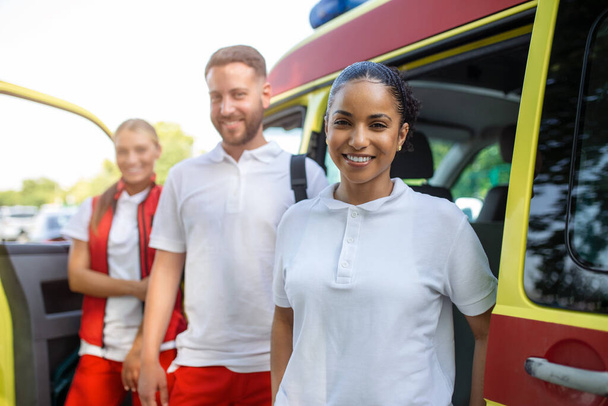 Paramédicos multiétnicos parados frente a una ambulancia. Médicos de emergencia y enfermeras de pie frente a la ambulancia - Foto, imagen