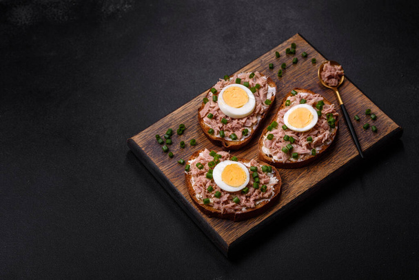 Delicious healthy sandwich with tuna, croutons, boiled egg, herbs and butter on a dark concrete background - Фото, изображение