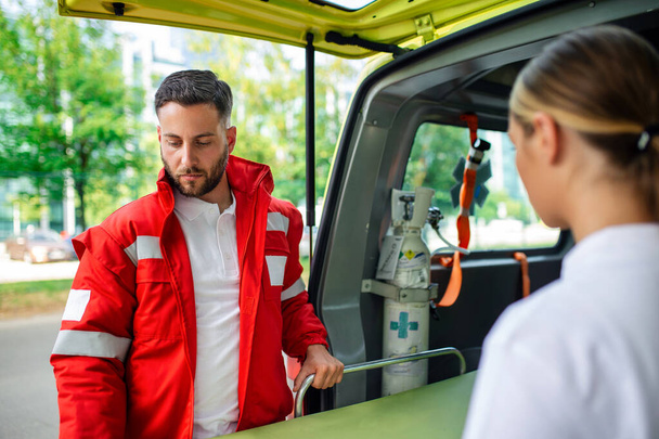 Zwei Sanitäter mit einer Trage in der Nähe eines Krankenwagens. Sanitäter in Uniform tragen Trage aus dem Rettungswagen - Foto, Bild