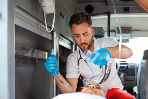 Doctor is ready for endotracheal intubation for non breathing patient. Young female paramedic holding iv solution. EMS Paramedics Provide Medical Help to an Injured Patient on the Way to a Hospital - Φωτογραφία, εικόνα