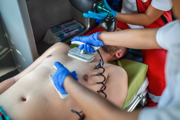 Rettungssanitäter leisten einem verletzten Patienten auf dem Weg in ein Krankenhaus medizinische Hilfe. Notfallhelfer setzen nicht-invasive Beatmungsmaske im Rettungswagen auf. - Foto, Bild