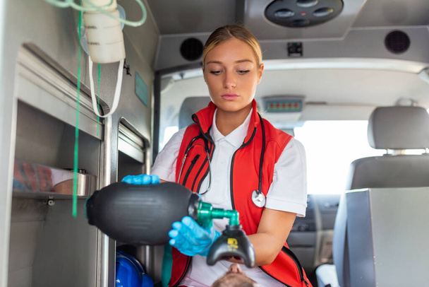 EMS Paramedics Provide Medical Help to an Injured Patient on the Way to a Hospital. Emergency Care Assistant Putting On Ventilation Mask with Silicone Manual Resuscitators in an Ambulance. - Photo, Image