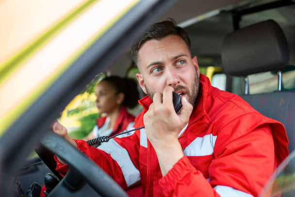 jóképű fiatal férfi mentős beszél hordozható rádió, miközben ül a mentőben - Fotó, kép