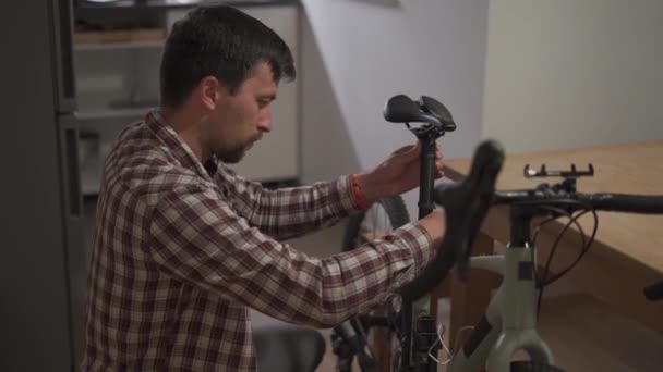 Muž doma opravuje kolo. Muž si doma opravuje kolo. Ten chlap si u nich doma upravuje kolo. Stavět kolo v malém bytě. Nastavení cyklu v malém ateliérovém pokoji - Záběry, video