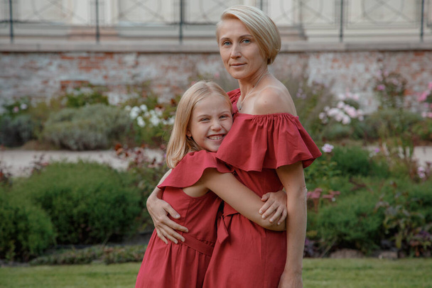 Mamá con su hija pequeña vestida como en vestido rojo. Joven madre y su niña se divierten. - Foto, Imagen