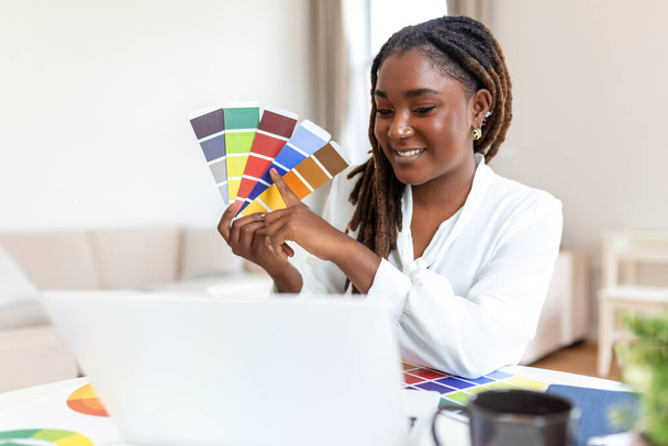 Vrolijk Afrikaans-Amerikaanse dame ontwerper met video conferentie met klanten, zitten aan het bureau in de voorkant van de computer, met kleurenpaletten, gebaren en glimlachen, kopieer ruimte - Foto, afbeelding