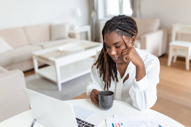 Vážná zamračená afroamerická etnická žena sedí u psacího stolu a dívá se na monitor notebooku a čte si e-maily. znuděný nemotivovaný unavený zaměstnanec, problémy s aplikací - Fotografie, Obrázek