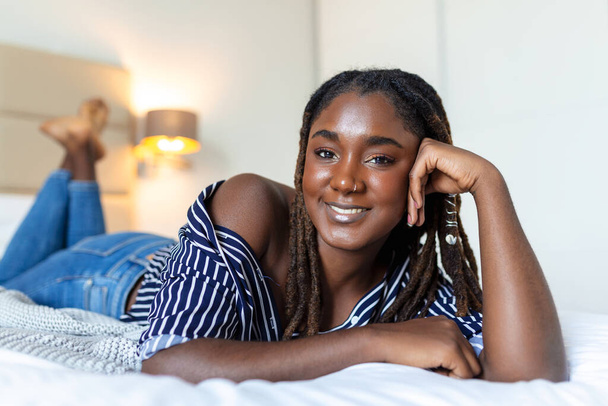 Porträt der schönen und sinnlichen jungen Afrikanerin, die auf dem Bett liegt. Schöne Frau liegt im Bett Afrikanische junge Frau liegt auf dem Bett. - Foto, Bild