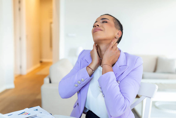Businesswoman feeling pain in neck after sitting at the table with laptop. Tired female suffering of office syndrome because of long hours computer work. Pretty girl massaging her tense neck muscles - Photo, image
