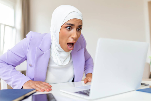 Confundido árabe musulmana mujer de negocios molesto por el problema en línea, correo electrónico spam o noticias falsas de Internet mirando a la computadora portátil, trabajador de oficina se siente sorprendido por la computadora atascada - Foto, Imagen