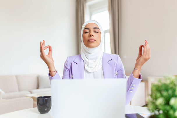 Calm Arabic muslim female executive meditating taking break at work for mental balance, mindful businesswoman feeling relief and no stress doing yoga at work ignoring avoiding stressful job - 写真・画像