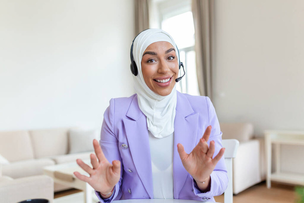Empresaria en Hijab teniendo un video chat en el portátil. Mujer sentada en la cafetería y haciendo videollamadas usando auriculares y computadora portátil. - Foto, imagen