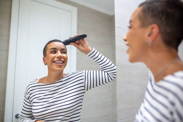 Reflejo espejo de mujer de pelo corto en camiseta con máquina de corte de pelo - Foto, imagen