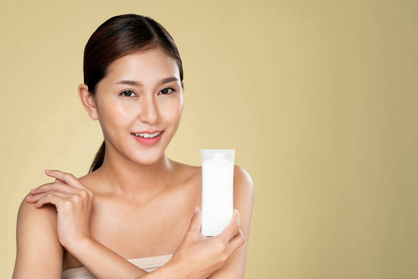 Жінка, яка посміхається, тримає макетний продукт для рекламного текстового місця, світло-сірого фону. Концепція охорони здоров'я для шкіри, косметичний засіб для реклами
. - Фото, зображення