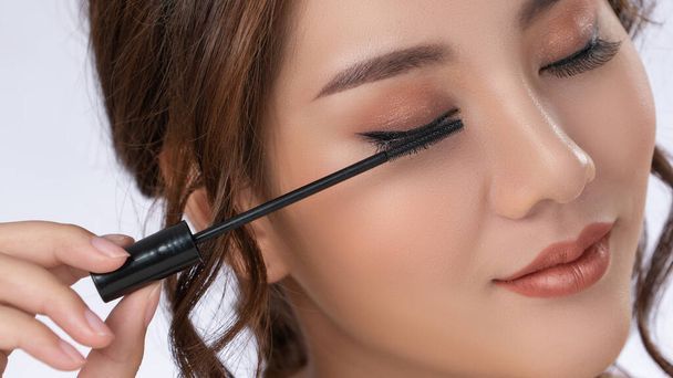 Closeup gorgeous young woman putting black mascara on her long eyelashes with brush. Beauty cosmetic concept. Female model with perfect skin. - Foto, Imagem