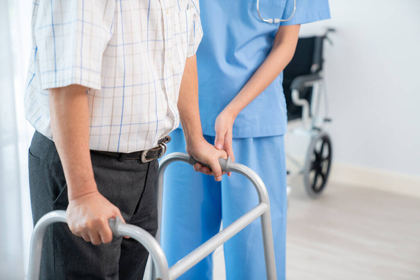 Physiotherapist assists contented senior man on folding walker. Recuperation for elderly, seniors care, nursing home. - Photo, image