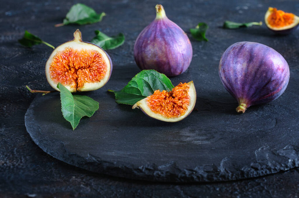 Fresh figs whole and cut into pieces on black slate. Autumn fruits. Front view, selective focus, daylight - Photo, Image