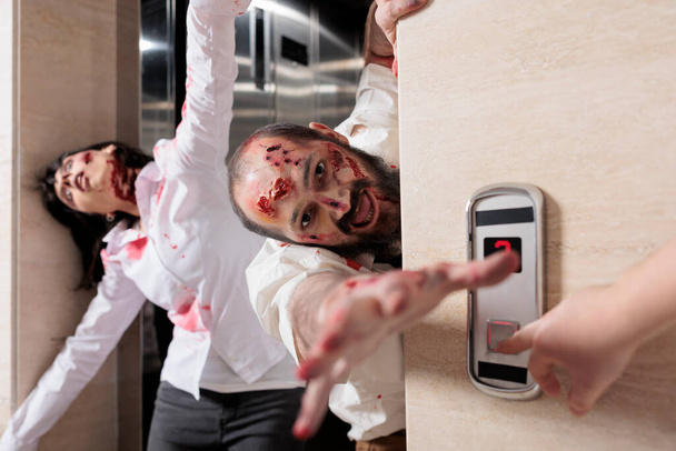 Porträt eines Zombie-Mannes, der sein Büro angreift, aus dem Fahrstuhl entkommt und mit blutigen Narben gefährlich aussieht. Unheimliche aggressive Monster, die Menschen erschrecken und ihnen hinterherjagen, hirnfressende Spaziergänger. - Foto, Bild
