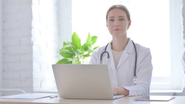 Женщина-врач смотрит в камеру, сидя в клинике - Фото, изображение