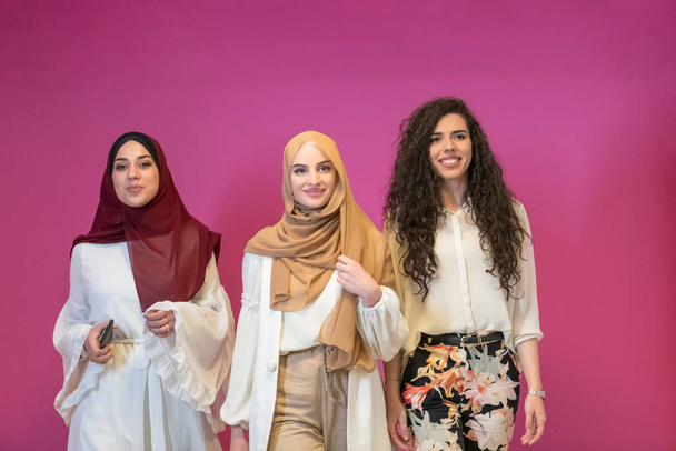 three Muslim women in hijab in modern clothes pose against a pink background.  - Фото, зображення
