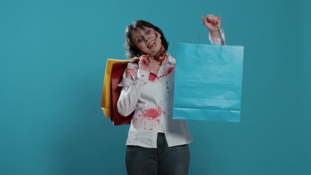 Zlověstná děsivá zombie s barevnými nákupními taškami z obchoďáku na modrém pozadí. Nebezpečná agresivní vypadající bezduchá chodící mrtvola s krvavými ranami držící zlevněné nákupy v obchoďáku. - Záběry, video