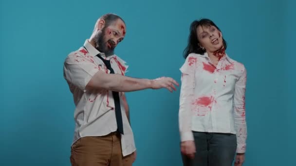 Funny scary looking office zombies touching each other and acting dumb in front of camera. Mindless brain-eating dead walking corpses with bloody and deep and scars acting childish on blue background. - Séquence, vidéo
