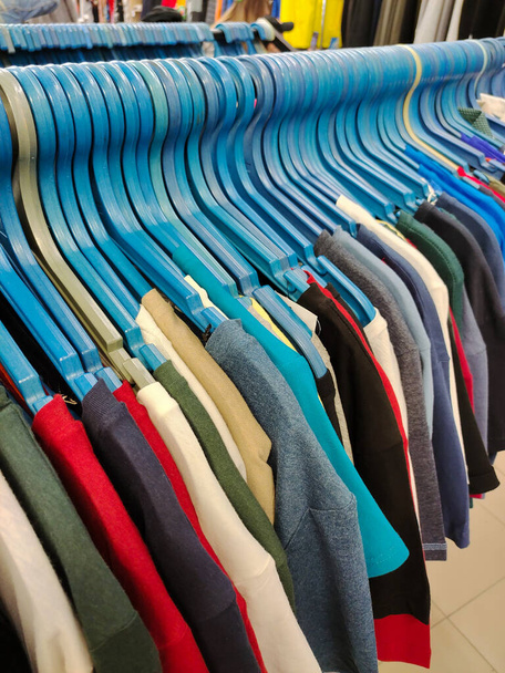 Rijen hangers met een breed scala aan kleurrijke t-shirts in een kledingwinkel in perspectief - Foto, afbeelding