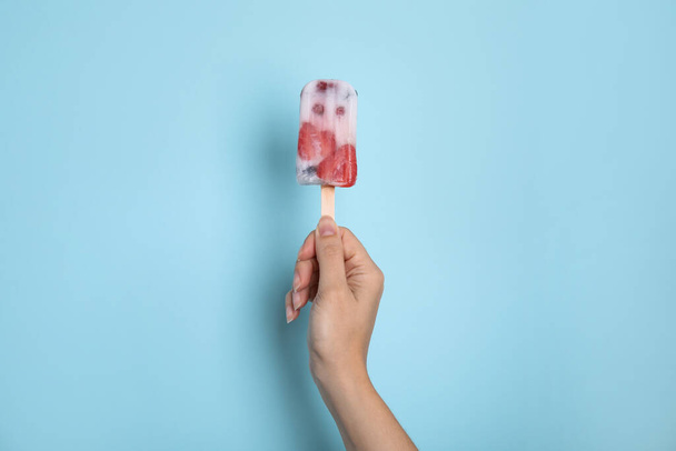 Woman holding berry popsicle on light blue background, closeup - Foto, immagini