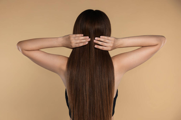 Young woman with strong healthy hair on beige background, back view - 写真・画像