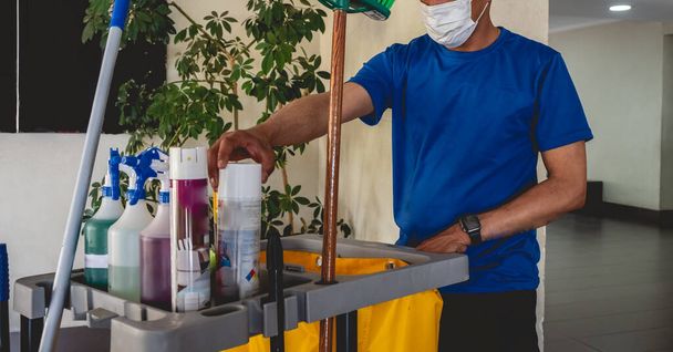 青色の制服を着た若いラティノの清掃員と道具と清掃用品(噴霧器、ほうき、掃除機など)) - 写真・画像