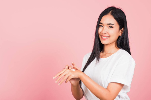 Portrait of Asian beautiful young woman applying lotion cosmetic moisturizer cream on her behind the palm skin back hand, studio shot isolated on pink background,  Hygiene skin body care concept - 写真・画像