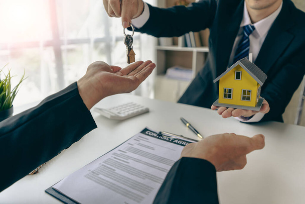 Agenti immobiliari e rappresentanti di vendita distribuiscono chiavi da nuove case a clienti d'ufficio con esempi di case disposte di fronte. - Foto, immagini