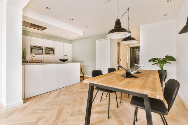 Kortárs minimalista stílusú belsőépítészeti világos stúdió apartman fa asztallal és székekkel étkező között nyitott konyha és nappali fehér falakkal és parketta padlóval - Fotó, kép