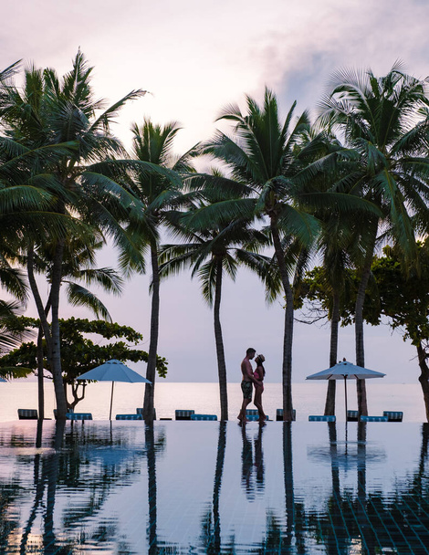 Pár mužů a žen odpočívajících u bazénu v plážových lehátkách, tropickém bazénu a bazénu s palmami na pláži s výhledem na oceán - Fotografie, Obrázek