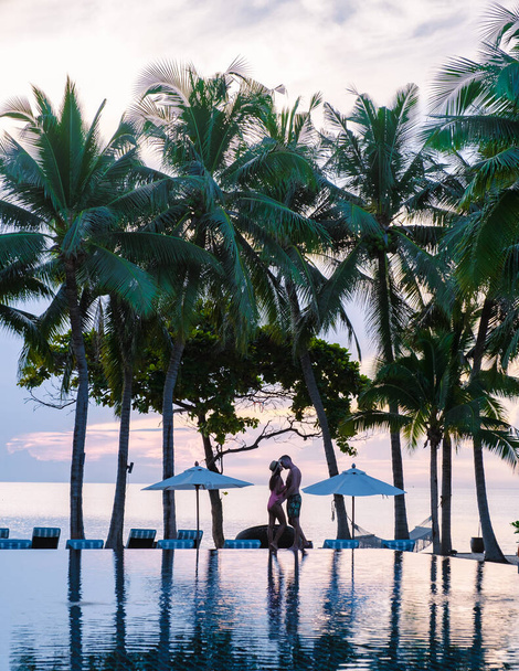 Een paar mannen en vrouwen ontspannen bij het zwembad in strandbedden stoelen, tropisch zwembad, en zwembad met palmbomen op het strand met uitzicht op de oceaan - Foto, afbeelding
