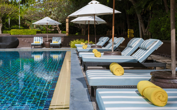 basen tropikalny z palmami i leżakami plażowymi w luksusowym kurorcie, basen z palmami na plaży z widokiem na ocean. krzesła plażowe z ręcznikiem plażowym przy basenie - Zdjęcie, obraz