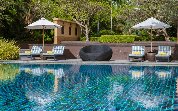 piscina tropicale con palme e sedie a sdraio in un resort di lusso, piscina con palme sulla spiaggia con vista sull'oceano. sedie a sdraio con telo mare in piscina - Foto, immagini