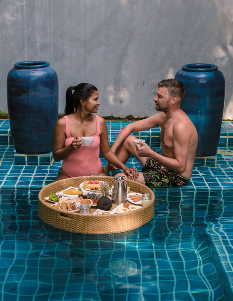 Um casal tomando café da manhã na piscina, mulheres asiáticas e homens caucasianos tomando café da manhã flutuante na piscina - Foto, Imagem