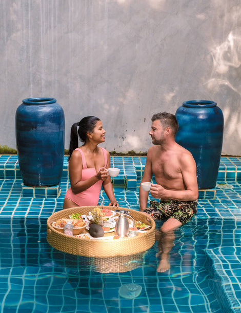 Una pareja desayunando en la piscina, mujeres asiáticas y hombres caucásicos desayunando flotando en la piscina - Foto, Imagen
